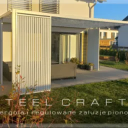 Biała, nowoczesna konstrukcja z regulowanymi żaluzjami pionowymi, tworząca zacienioną przestrzeń na tarasie, z widocznym zestawem mebli wypoczynkowych i zadbanym trawnikiem w tle.