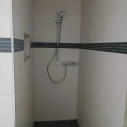 Wykończona kabina prysznicowa z beżowymi płytkami z ciemnym paskiem dekoracyjnym i czarną podłogą, widok z góry.