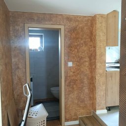 URB Krzysztof Kochanowski - Wnętrze mieszkania po nałożeniu dekoracyjnej, brązowej farby strukturalnej na ścianach, widoczne wejście do łazienki i fragment zabudowy kuchennej.