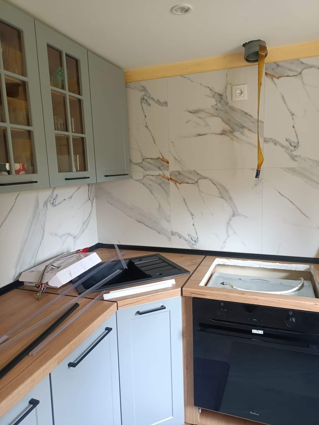 Montaż zlewozmywaka i płyty indukcyjnej w kuchni: widoczne podłączenia hydrauliczne, elementy wykończeniowe i fragment marmurowej ściany nad blatem.