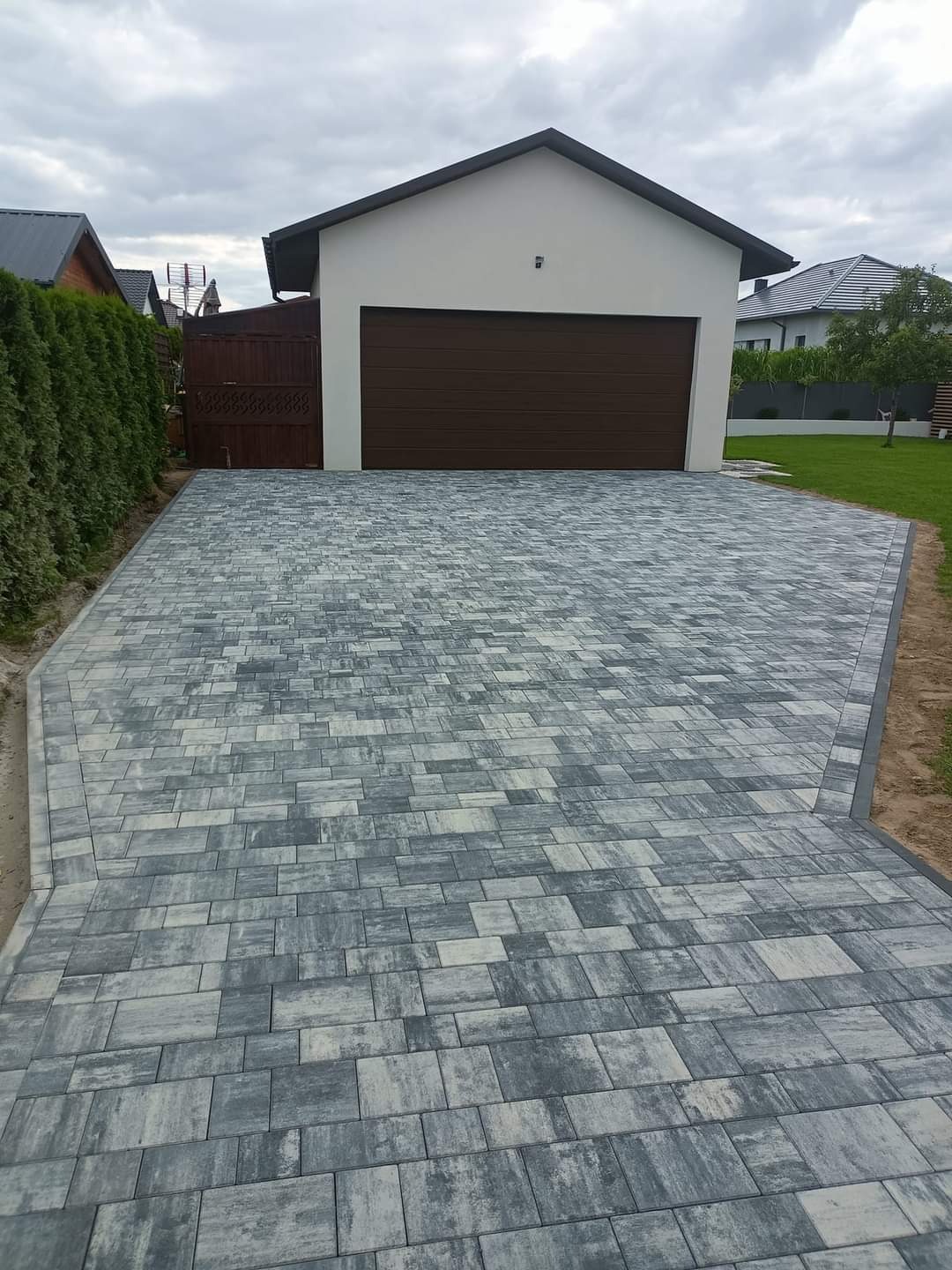 Ułożona szara kostka brukowa prowadząca do garażu z brązową bramą, widok z góry, pochmurne niebo.