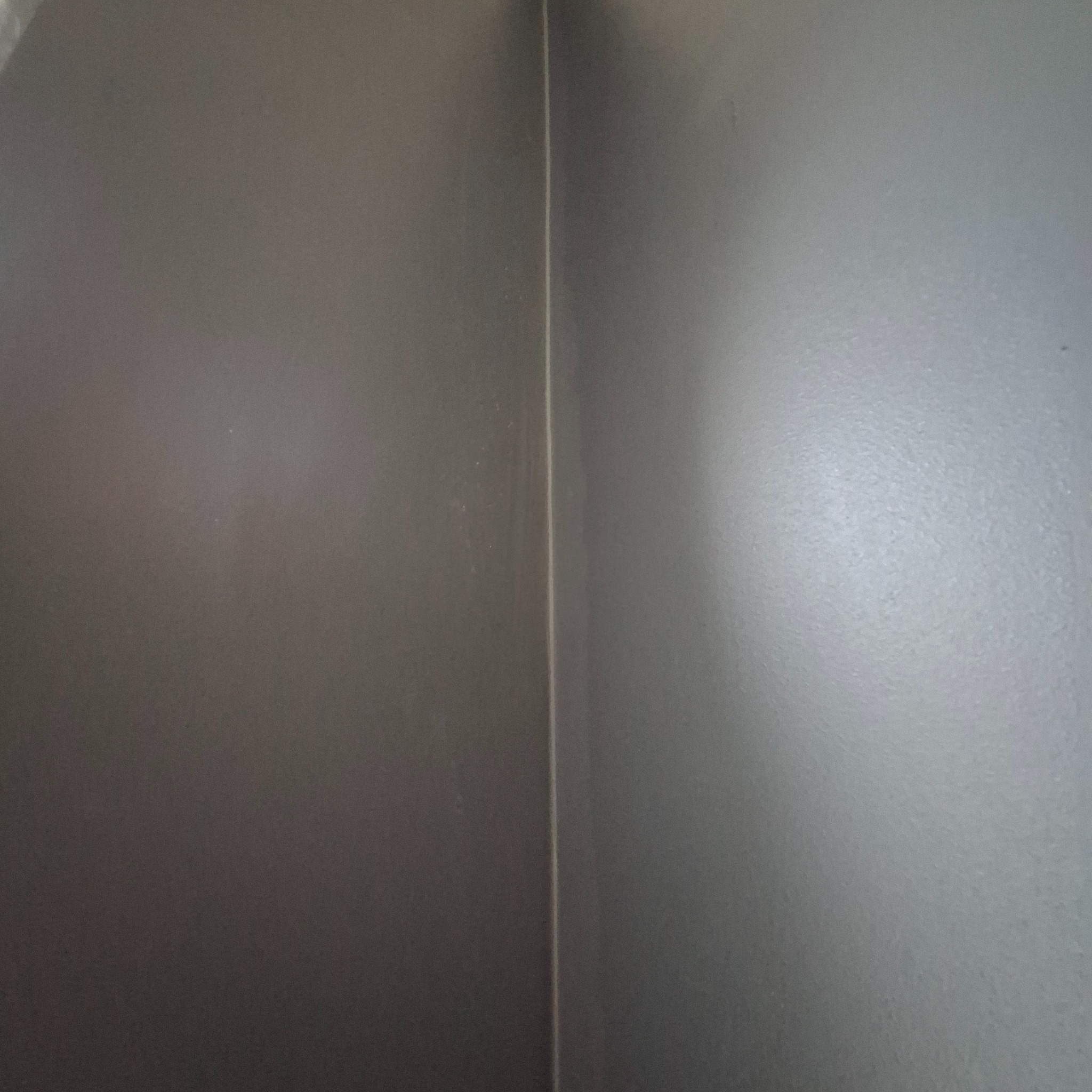 Szara ściana po szpachlowaniu i malowaniu, widoczny narożnik z delikatnym przejściem kolorystycznym pod różnym kątem padania światła.