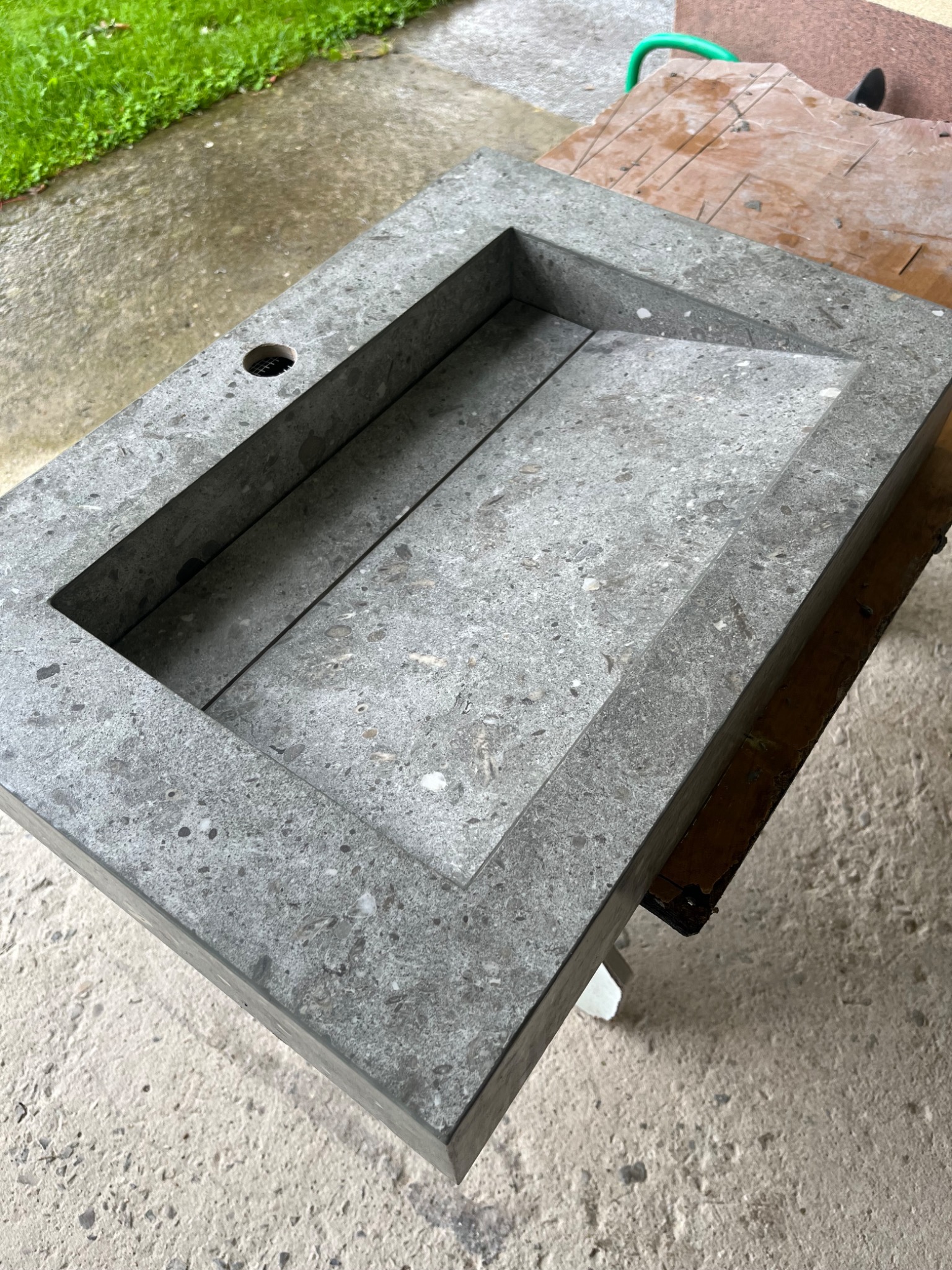 Szary, kamienny blat umywalkowy z otworem na baterię, o fakturze lastryko, leżący na drewnianym stole roboczym.