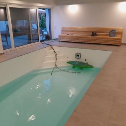 Fhu Ren Dam - Wnętrze z basenem: jasne płytki podłogowe, białe ściany, drewniana ławka. W basenie pływa dmuchany krokodyl. Widoczne schody wejściowe i akcesoria do czyszczenia.