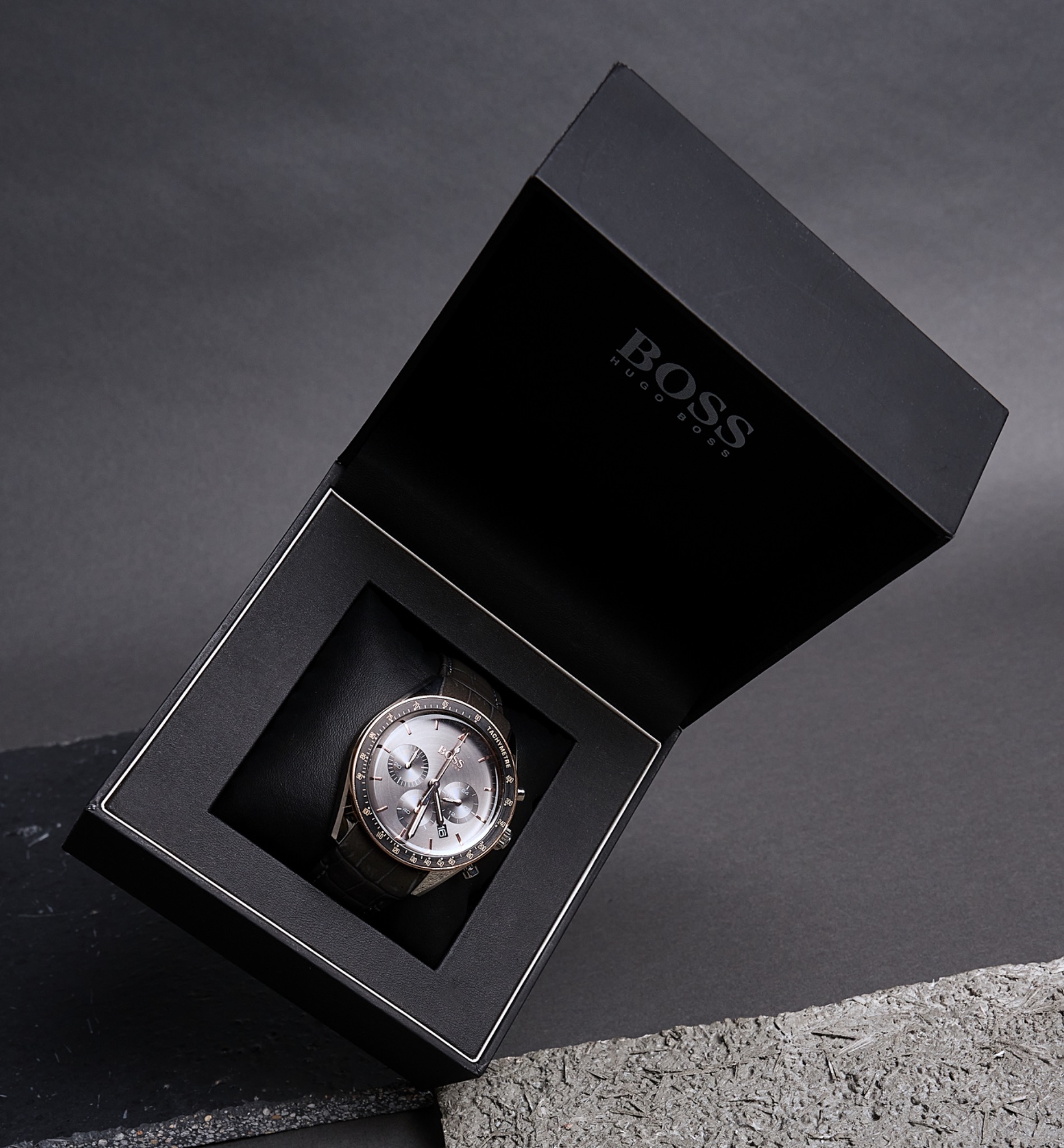 Elegancki zegarek męski marki Boss w otwartym, czarnym pudełku na tle szarej powierzchni.