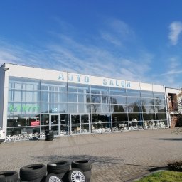 Świat felg i opon - Auto Salon Kubeczek z ekspozycją opon i felg przed budynkiem w słoneczny dzień.