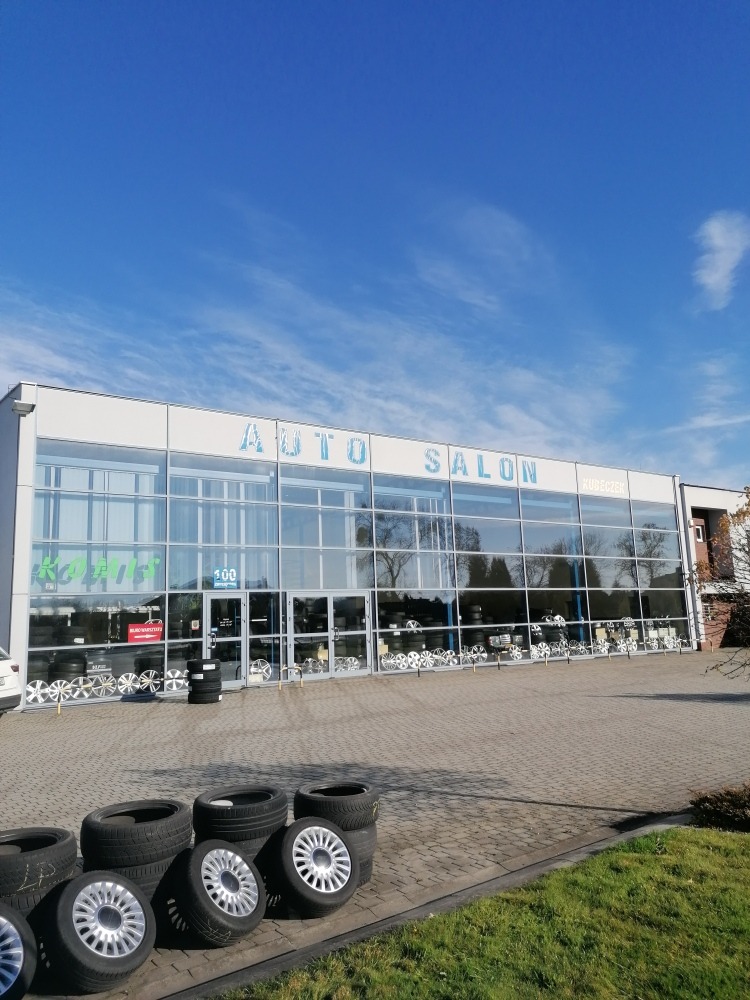 Auto Salon Kubeczek z ekspozycją opon i felg przed budynkiem w słoneczny dzień.
