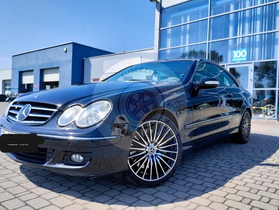 Czarny Mercedes CLK z nowymi felgami aluminiowymi, zaparkowany przed nowoczesnym budynkiem z przeszkloną fasadą w słoneczny dzień.