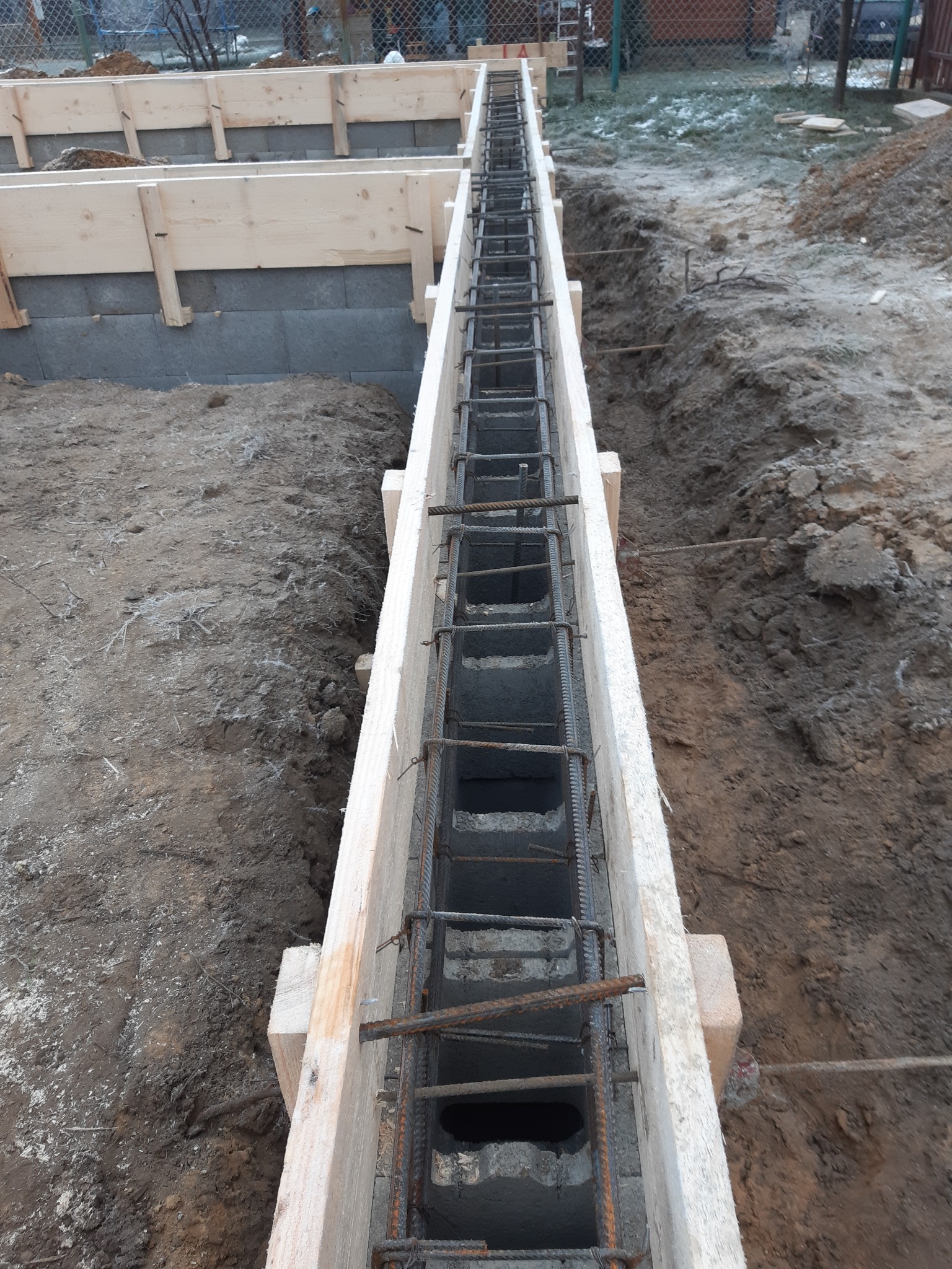 Szalunek zbrojeniowy przygotowany do wylewania fundamentów na działce z ziemią i fragmentami śniegu.