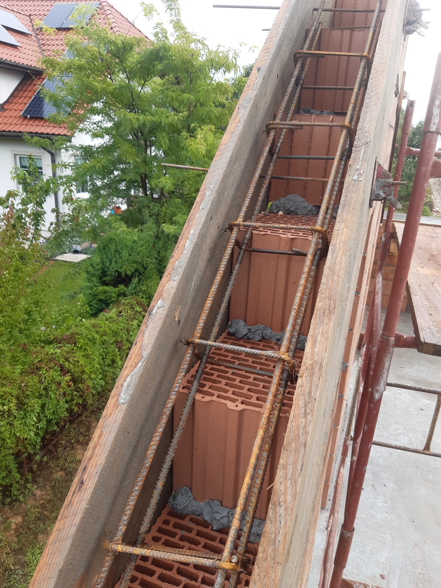 Zbrojenie pionowe ściany z pustaków ceramicznych, zalewane betonem, widoczne szalunki drewniane i fragment rusztowania.
