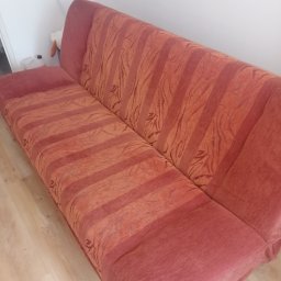 Czyszczenie tapicerki meblowej - Rozłożona, pomarańczowo-czerwona kanapa z wzorem w paski i liście, ustawiona na jasnej podłodze, widoczna z boku.