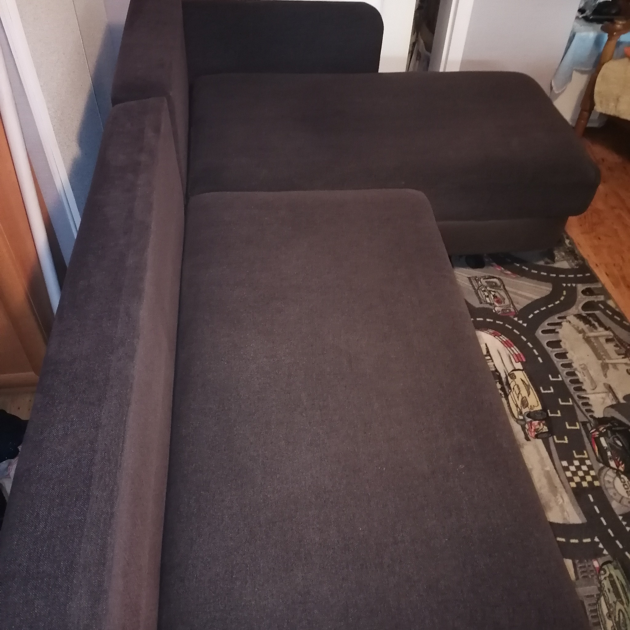 Ciemnoszara, narożna kanapa z tapicerką z bliska, ustawiona na dywanie z motywem samochodów i ulic.