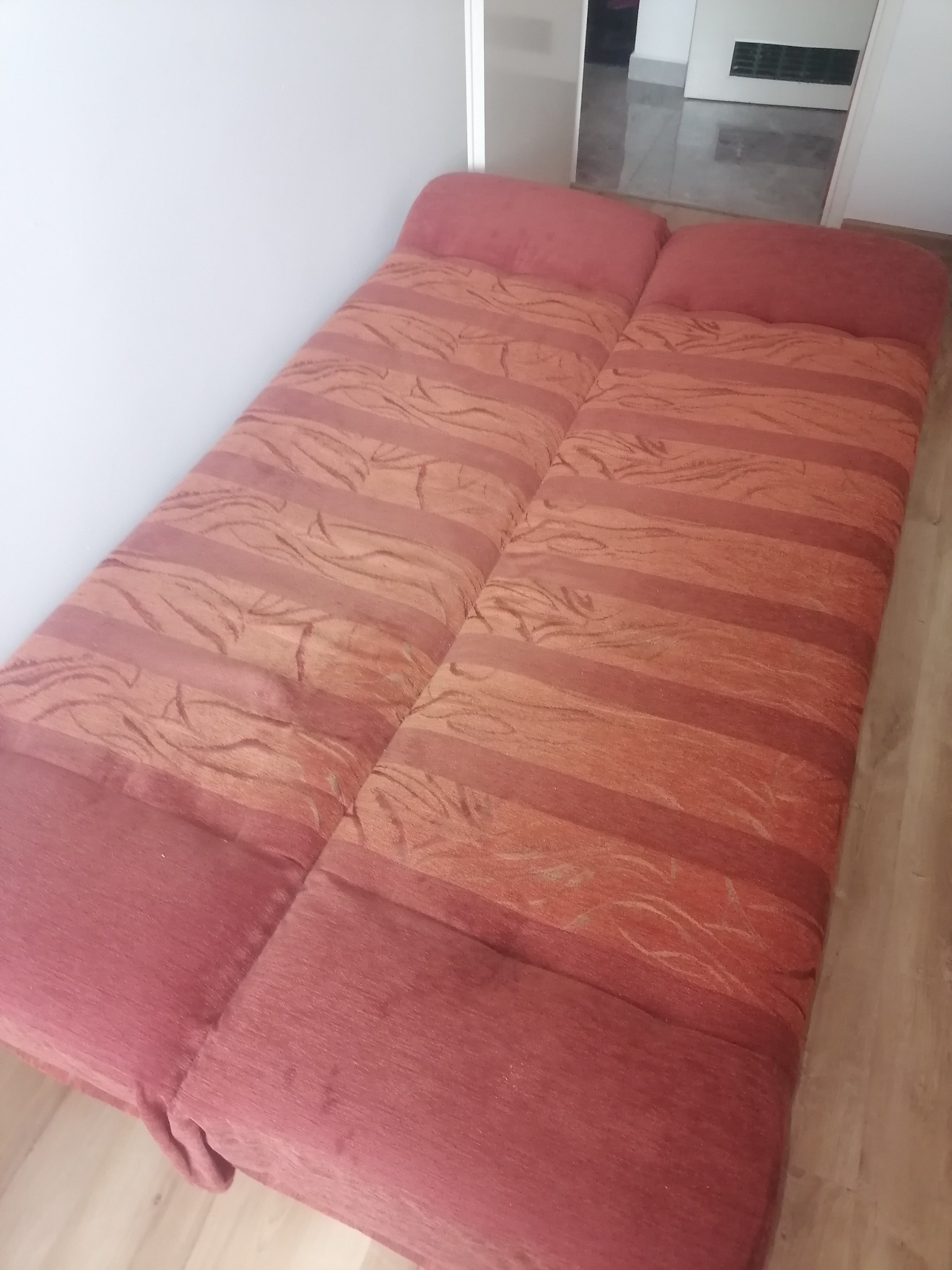 Rozłożona, dwuczęściowa kanapa w odcieniach czerwieni i pomarańczy, z wzorem w paski i liście, widoczna na tle podłogi w Szczecinie.