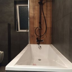 Prestige Tiling - Nowoczesna łazienka z wanną w zabudowie, czarna armatura, drewnopodobne panele na ścianie i uchylne okno.