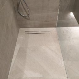 Prestige Tiling - Nowoczesny prysznic walk-in z odpływem liniowym i szarymi płytkami imitującymi kamień, widoczne krople wody na szklanej ściance.