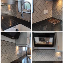 Wykończona kuchnia z szarymi płytkami ułożonymi w jodełkę na ścianie nad czarnym, błyszczącym blatem, widoczny zlew, bateria i okap.