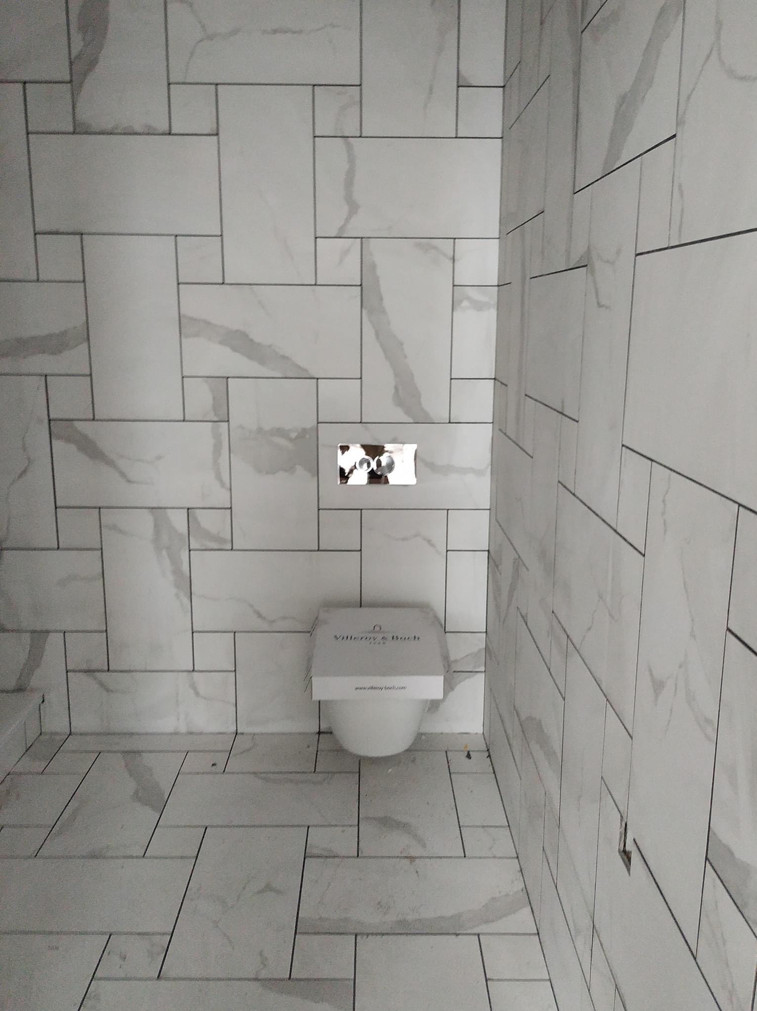 Nowoczesna łazienka z białymi płytkami imitującymi marmur, ułożonymi w nieregularny wzór, z wiszącą miską WC marki Villeroy & Boch i chromowanym przyciskiem spłukującym.