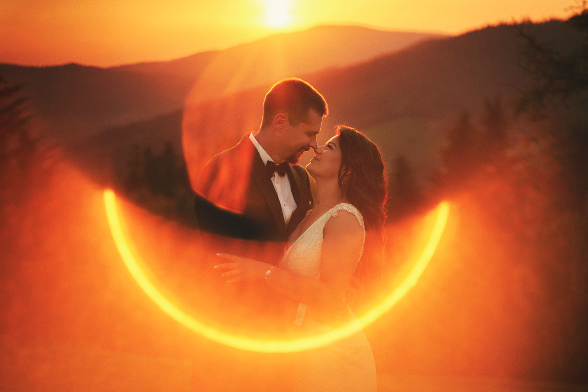 Para młoda w objęciach na tle górskiego krajobrazu o zachodzie słońca, z efektem bokeh w kształcie półksiężyca.