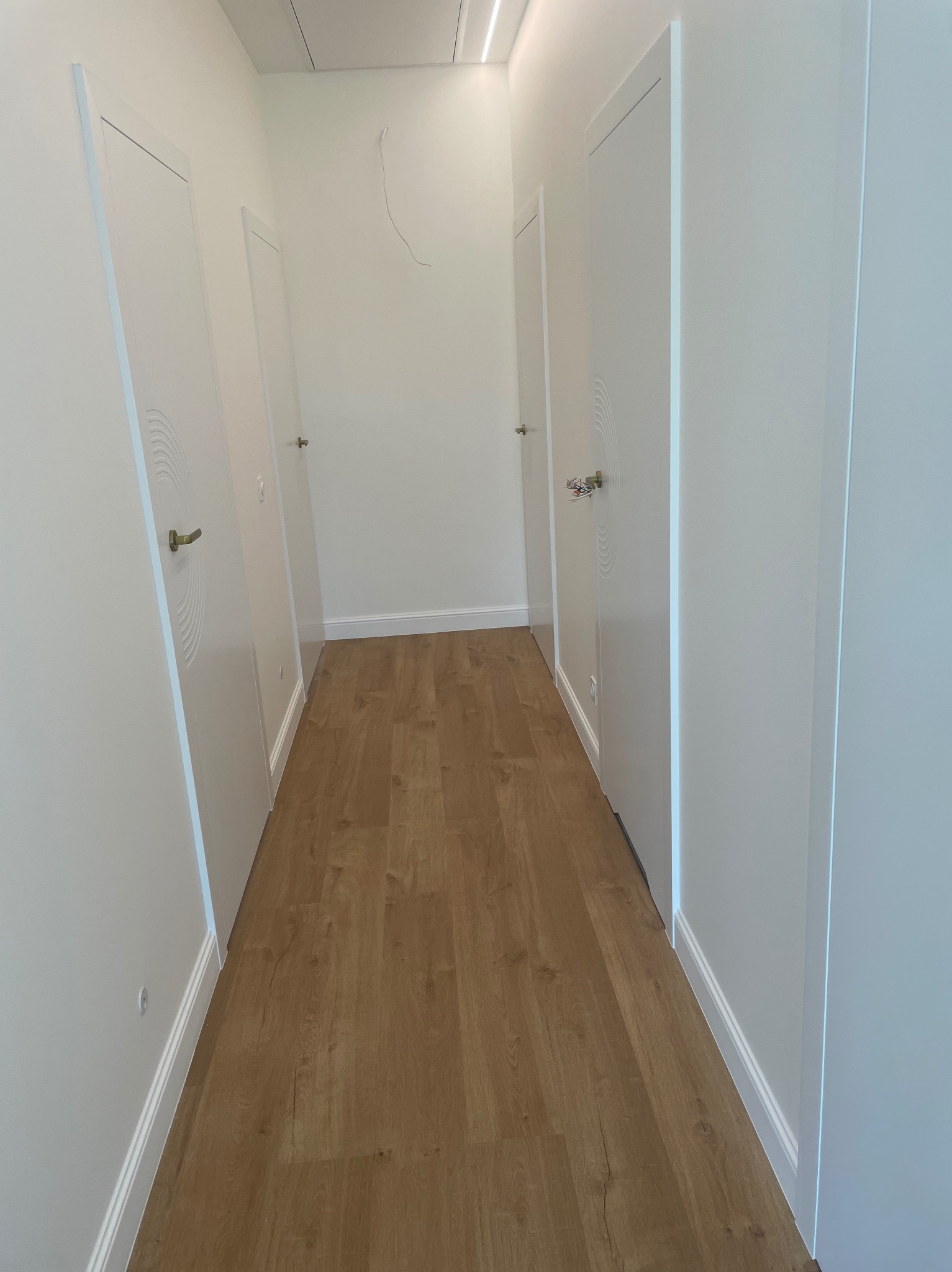 Korytarz z trzema białymi skrzydłami drzwiowymi z dekoracyjnym, frezowanym motywem półokręgów, widoczne złote klamki i panele podłogowe w odcieniach brązu.