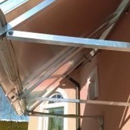 AGO Tomasz Stawowy - Zewnętrzna markiza przeciwsłoneczna z aluminiową konstrukcją zamontowana nad oknem na beżowej elewacji budynku.