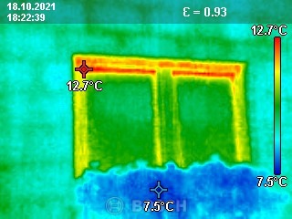 Termowizyjne zdjęcie okna, ukazujące rozkład temperatur. Ciepło uciekające przez ramę okienną zaznaczone kolorem pomarańczowym i czerwonym, chłodniejsza szyba w odcieniach zieleni i błękitu.