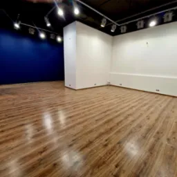 Puste, odnowione wnętrze biurowe z drewnianą podłogą, świeżo pomalowanymi ścianami w kolorze białym i granatowym, oraz nowoczesnym oświetleniem punktowym na suficie.