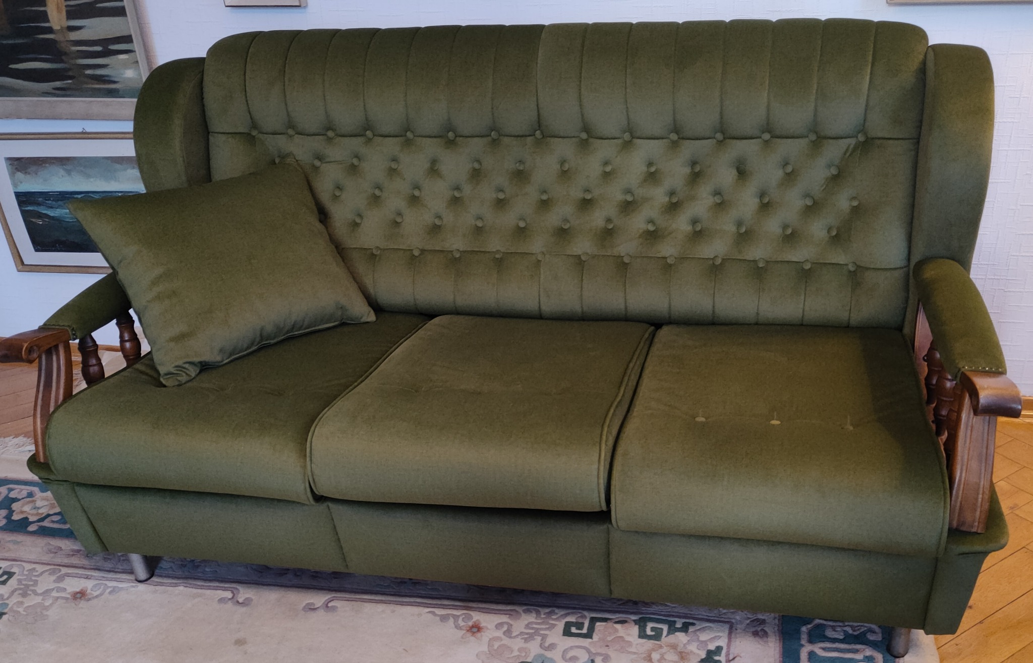 Odrestaurowana sofa w odcieniach zieleni z drewnianymi elementami, widoczna poduszka i pikowane oparcie, stojąca na wzorzystym dywanie.