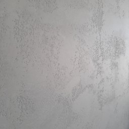 GENERAL HELP Sp.z.o.o - Szara ściana z dekoracyjną, chropowatą fakturą i delikatnym połyskiem, oświetlona z prawej strony.