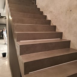 GENERAL HELP Sp.z.o.o - Betonowe schody z wbudowanym oświetleniem LED na każdym stopniu, malarz w kombinezonie w tle, surowa betonowa ściana obok