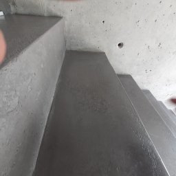 GENERAL HELP Sp.z.o.o - Surowe betonowe schody wewnętrzne w trakcie budowy, widoczne niedoskonałości powierzchni i sufit z widocznymi otworami.