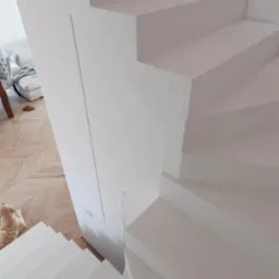 Wnętrze domu z białymi, spiralnymi schodami widzianymi z góry, parkiet w jodełkę na podłodze i leżący pies rasy golden retriever.