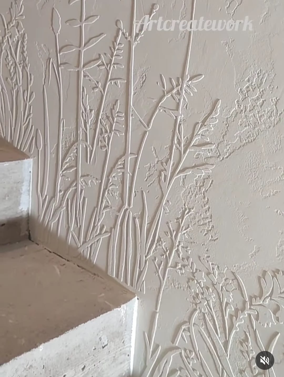 Wypukła dekoracja ścienna w odcieniach bieli, przedstawiająca motyw roślinny w pobliżu schodów, z widoczną fakturą tynku.