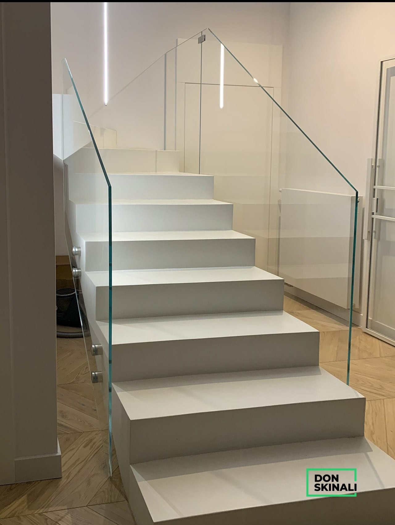 Nowoczesne, minimalistyczne schody w Warszawie z białymi stopniami i szklaną balustradą, oświetlone ledowymi lampami sufitowymi.