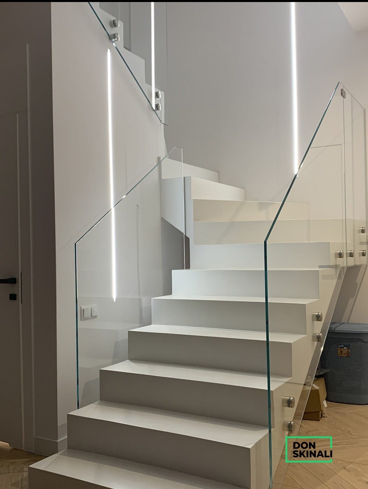 Nowoczesne, białe schody z przezroczystą szklaną balustradą i subtelnym oświetleniem LED wzdłuż ściany.