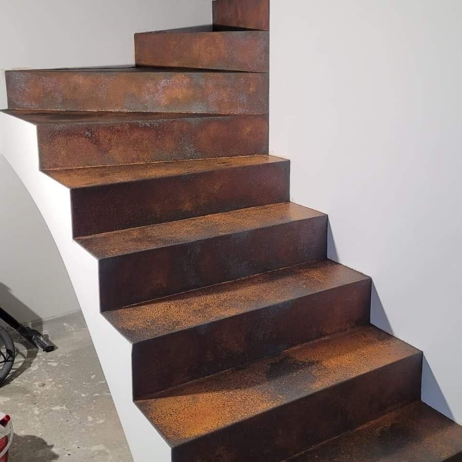 Schody wewnętrzne z efektem rdzy, białe boki, widok z dołu, fragment roweru w tle.