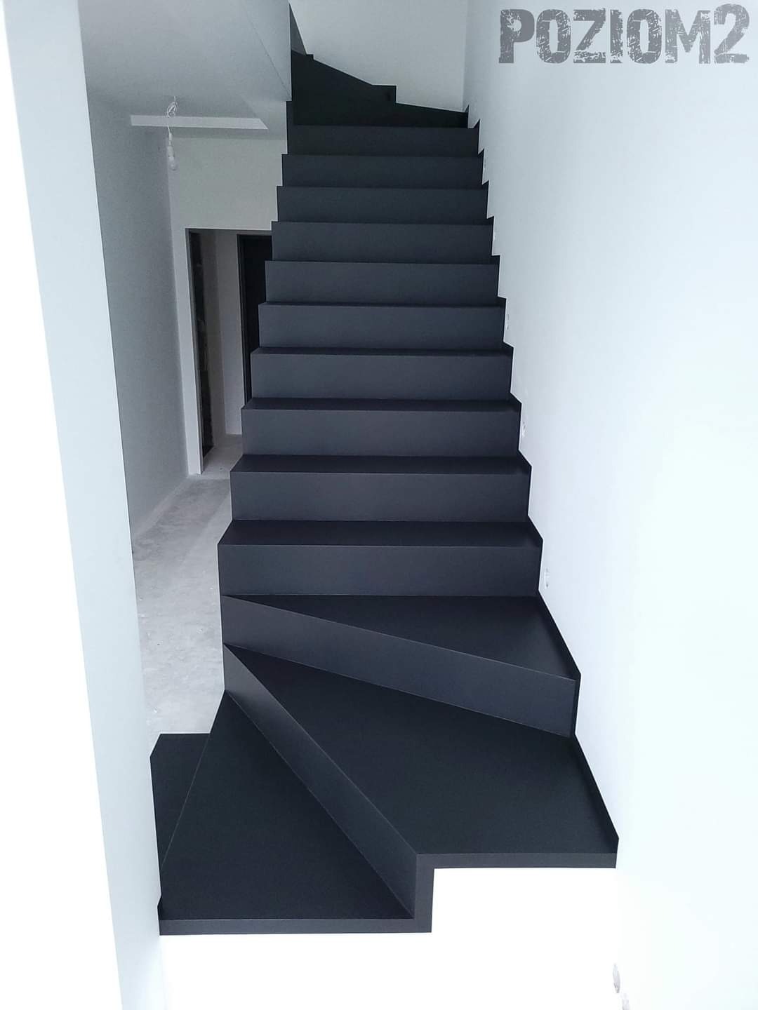 Nowoczesne, czarne schody zabiegowe bez poręczy prowadzące na wyższą kondygnację w jasnym wnętrzu z napisem 'POZIOM2' na ścianie.
