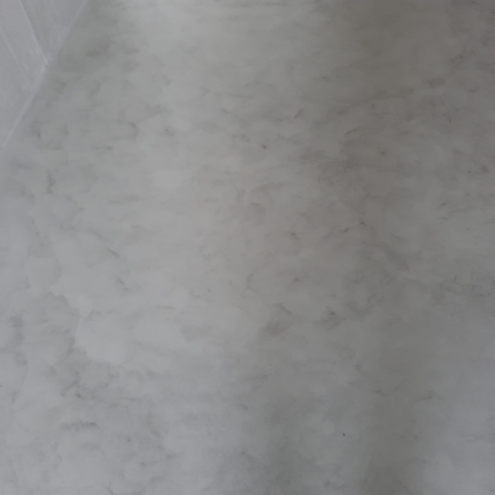 Szara, marmurkowa faktura ściany wewnątrz pomieszczenia, z delikatnym połyskiem i subtelnymi przejściami tonalnymi.