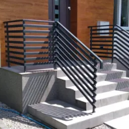 Nowoczesne, czarne balustrady schodowe z poziomych profili na zewnątrz budynku z drewnianą elewacją i szarymi schodami.