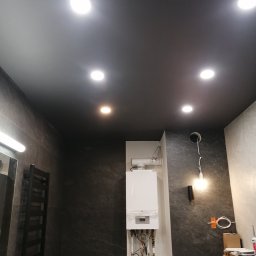 YA COMPANY SPÓŁKA Z OGRANICZONĄ ODPOWIEDZIALNOŚCIĄ - Ciemny sufit z oświetleniem punktowym w łazience z kamiennymi płytkami, widoczny bojler i grzejnik drabinkowy