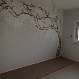 Ściana w pokoju w Warszawie z ręcznie malowanym motywem drzewa kwitnącej wiśni, widoczne puszki z farbą na parapecie okna.