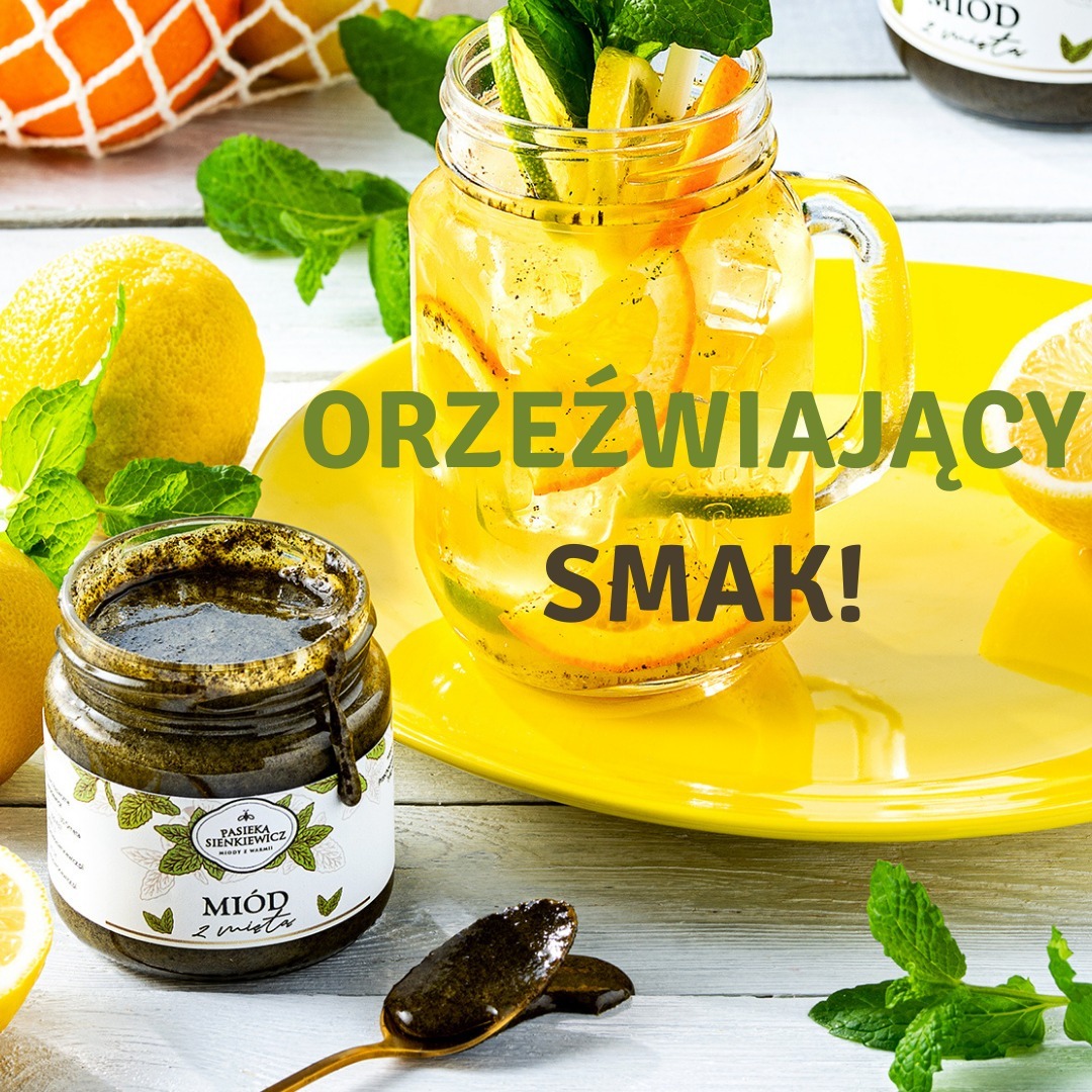 Słoik ciemnego miodu z miętą obok lemoniady cytrusowej z miętą na żółtym talerzu, z łyżką miodu i dekoracją z owoców i ziół.