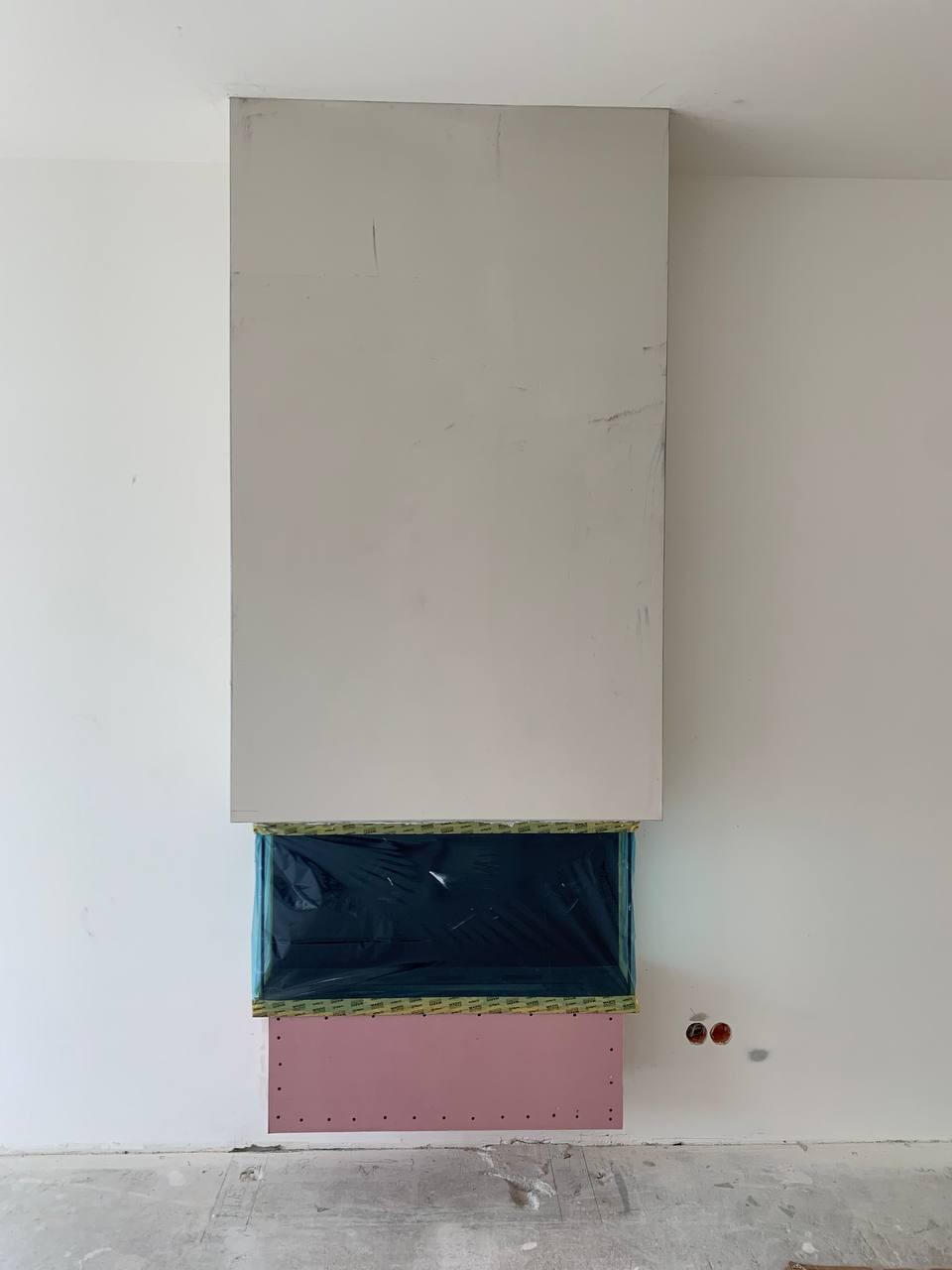 Przygotowanie ściany pod zabudowę kominka: płyta karton-gips, folia ochronna i taśma maskująca, widoczne gniazdka elektryczne na ścianie.