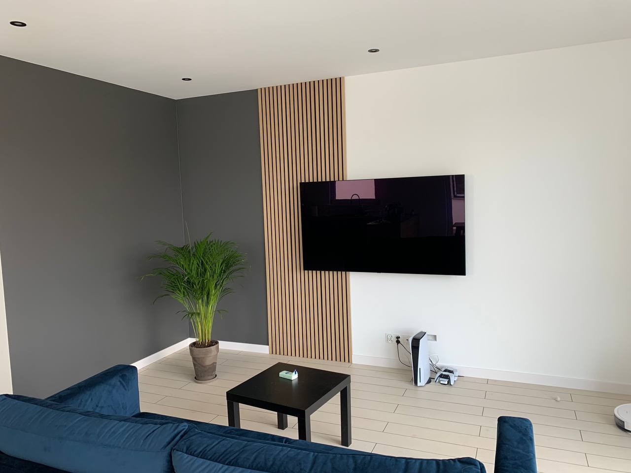 Nowoczesny salon w Szczecinie z szarą ścianą, drewnianymi panelami ściennymi, telewizorem, konsolą PlayStation 5 i niebieską sofą.