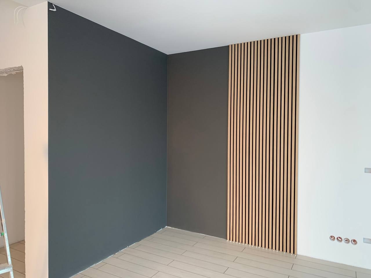 Wnętrze pokoju z szarą ścianą, drewnianymi lamelami ściennymi i białymi elementami, wykończone w nowoczesnym stylu.