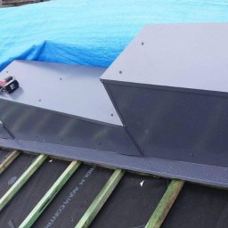 Ma-Bud - Szare, metalowe obróbki kominowe na dachu pokrytym membraną i łatami, zabezpieczone niebieską plandeką, narzędzia na górze.