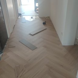 RN-BUD REMIGIUSZ ZDANOWICZ - Fragment podłogi z ułożonymi panelami w jodełkę, kilka paneli leży luzem, widoczny młotek gumowy i listwa przypodłogowa