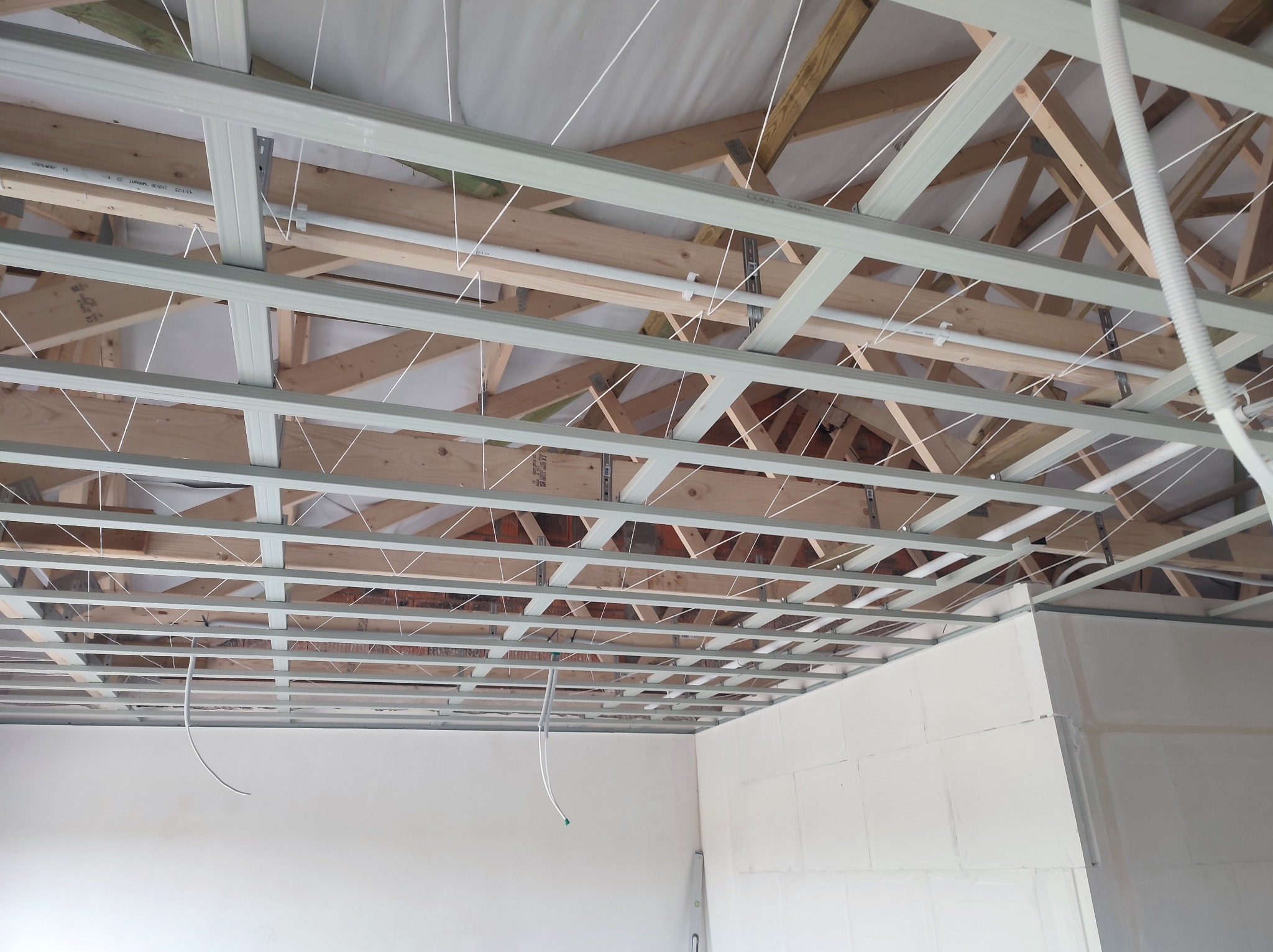 Konstrukcja sufitu podwieszanego z metalowych profili na drewnianej więźbie dachowej, widoczne przewody elektryczne i fragmenty ścian pokryte gładzią