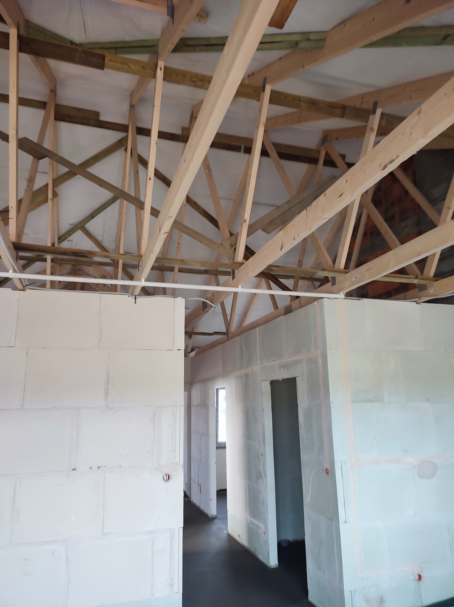 Wnętrze w stanie surowym: ściany z białych bloczków, drewniana konstrukcja dachu, widoczne instalacje elektryczne, posadzka w ciemnym kolorze.