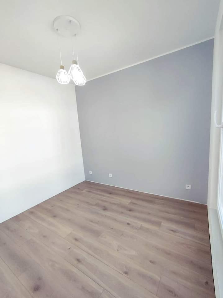Pusty pokój po remoncie z panelami podłogowymi w odcieniach brązu i szarości, ściany pomalowane w dwóch kolorach: biały i szary, nowoczesne lampy wiszące.
