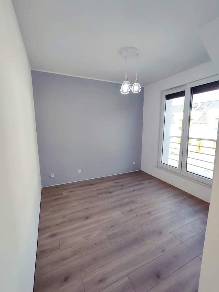 Pomalowane na szaro wnętrze pokoju z panelami podłogowymi, białymi ścianami i dwoma lampami wiszącymi w stylu industrialnym.